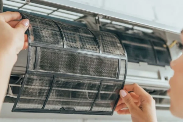 Persona limpiando los filtros del aire acondicionado en casa para mejorar la calidad del aire y la eficiencia energética